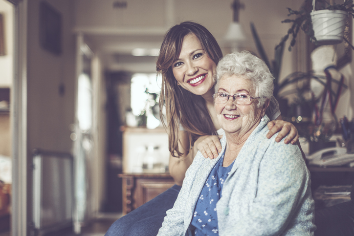 Elderly woman smiling with a woman embracing her shoulders